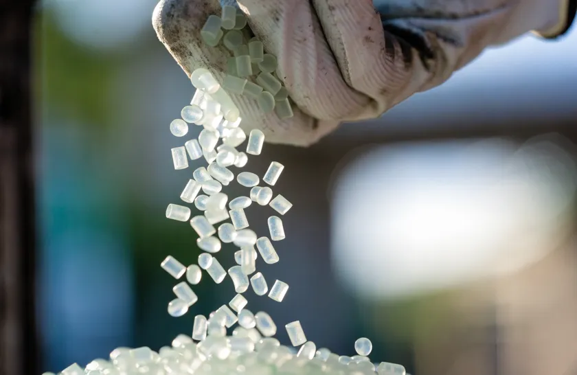 Pellets de polietileno reciclado cayendo de una mano enguantada